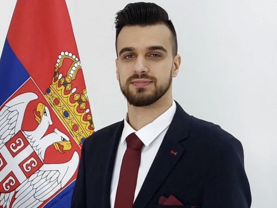 Marko Simić u poslovnom odelu ispred zastave Srbije